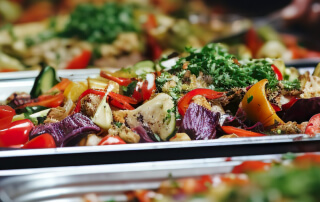 Bandeja de legumes assados, incluindo pimentões vermelhos, cebolas roxas, abobrinhas e outros vegetais temperados, cobertos com ervas frescas.