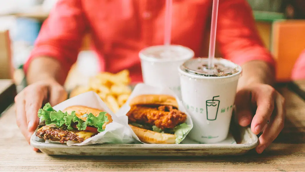 Hamburgueria fast-food servindo bandeja com hambúrguer de frango frito, batatas fritas e refrigerantes.