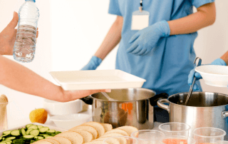 Profissional servindo bandeja com alimentos, ilustrando a gestão da alimentação hospitalar.